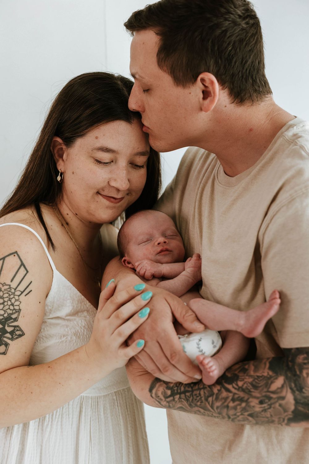 Intimate family moment as loving parents share tender moment with their newborn baby in soft lighting.