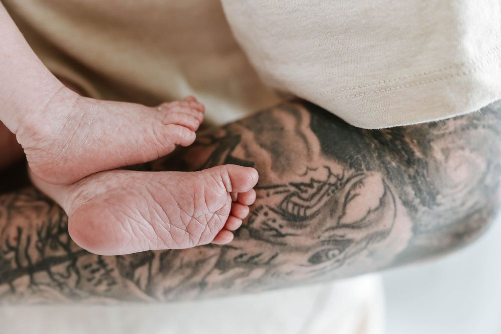 Tiny baby feet rest gently on a tattooed arm creating a touching contrast between new life and body art.