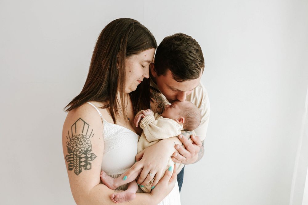 Parents lovingly embrace their newborn baby against a minimalist white background.
