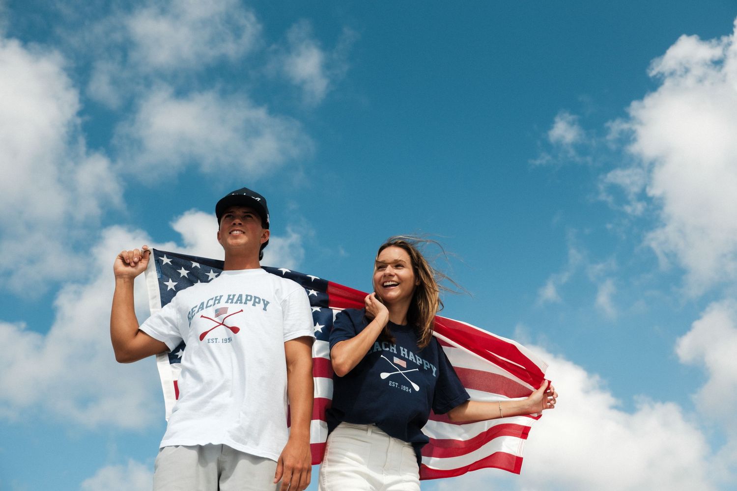 People holding American flag against bright blue sky with white clouds.