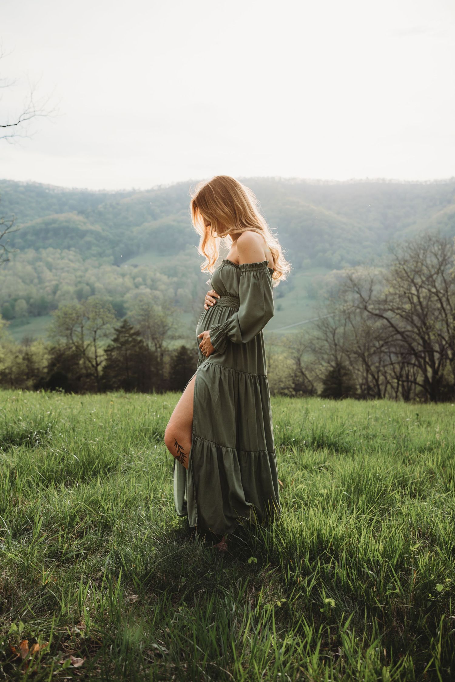 Artistic maternity photography in a scenic mountain field with tall grass.