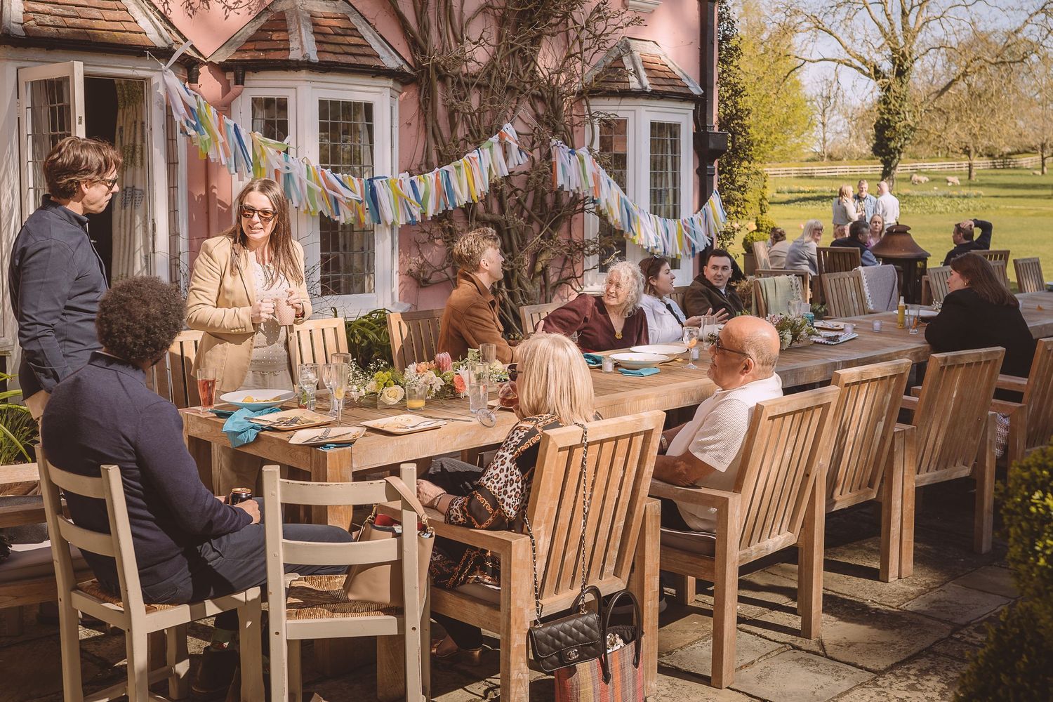 People enjoying the wedding catering on a wooden patio with bunting decorations on a sunny spring day.