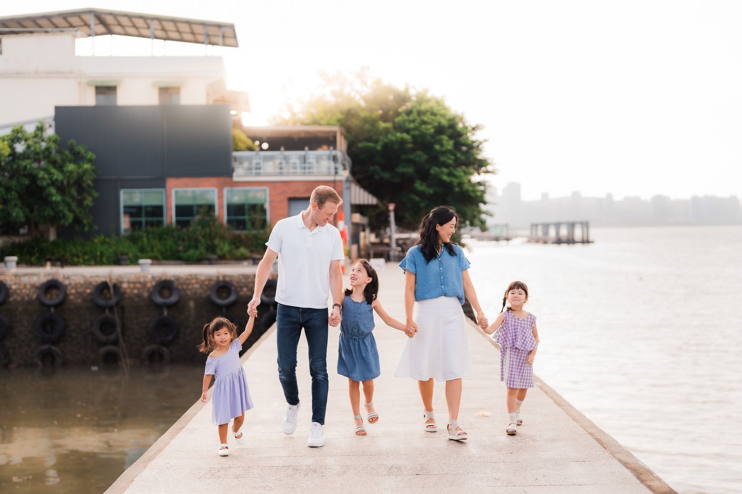 A family enjoys a playful moment lifting their child together under lush green trees in a peaceful park setting.