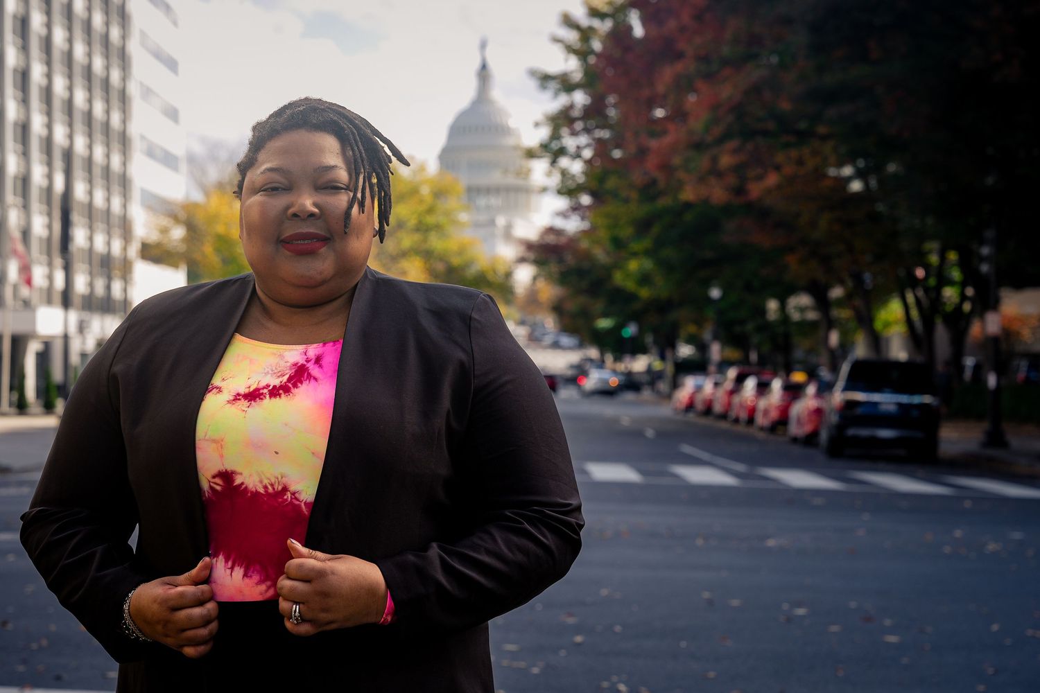 Professional in a vibrant pink blazer and white blouse smiling warmly against a dark gray background.