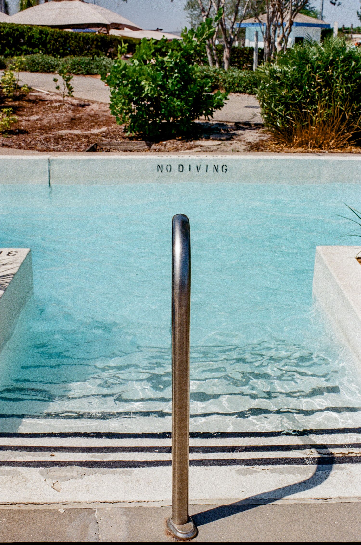 A stainless steel pool handrail next to clear blue water with 'NO DIVING' text visible on the pool edge.
