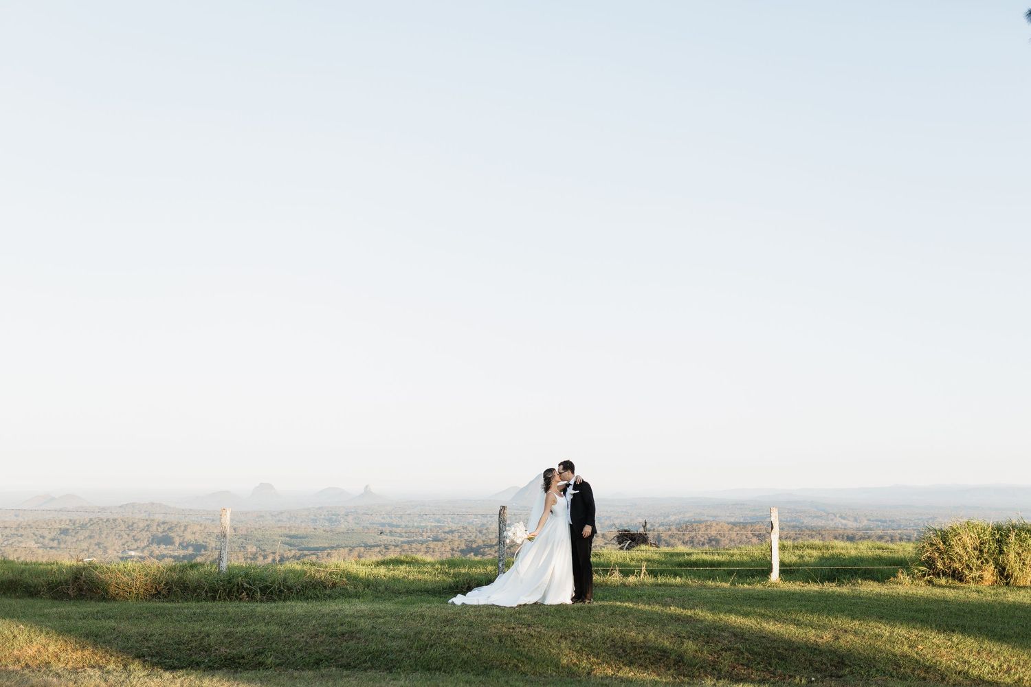 A couple poses together on a hilltop with scenic countryside views during their sunset wedding photoshoot.