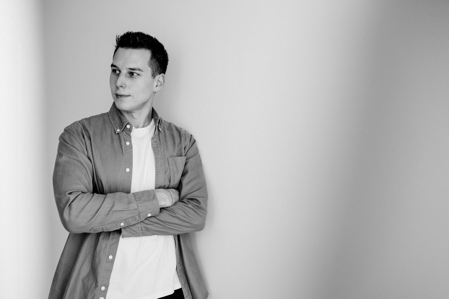 A black and white portrait of someone in a casual jacket and t-shirt standing against a plain wall with arms crossed.Business Portrait