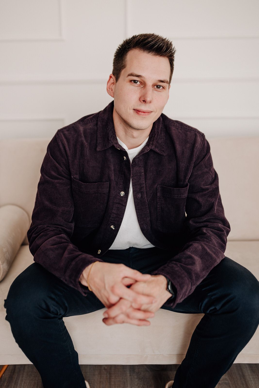 Someone in a dark jacket sits casually on a white couch with hands clasped.Business Portrait Rheinmain Frankfurt