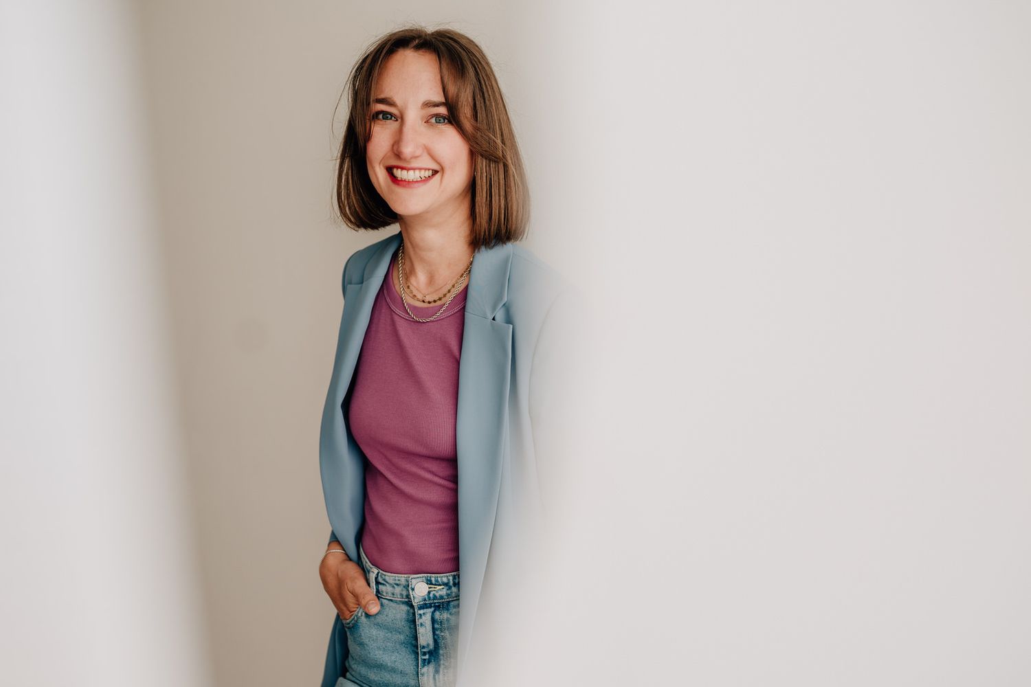 Professional in light blue blazer and pink top poses against white wall with confident smile.Business Portrait Rheinmain Frankfurt