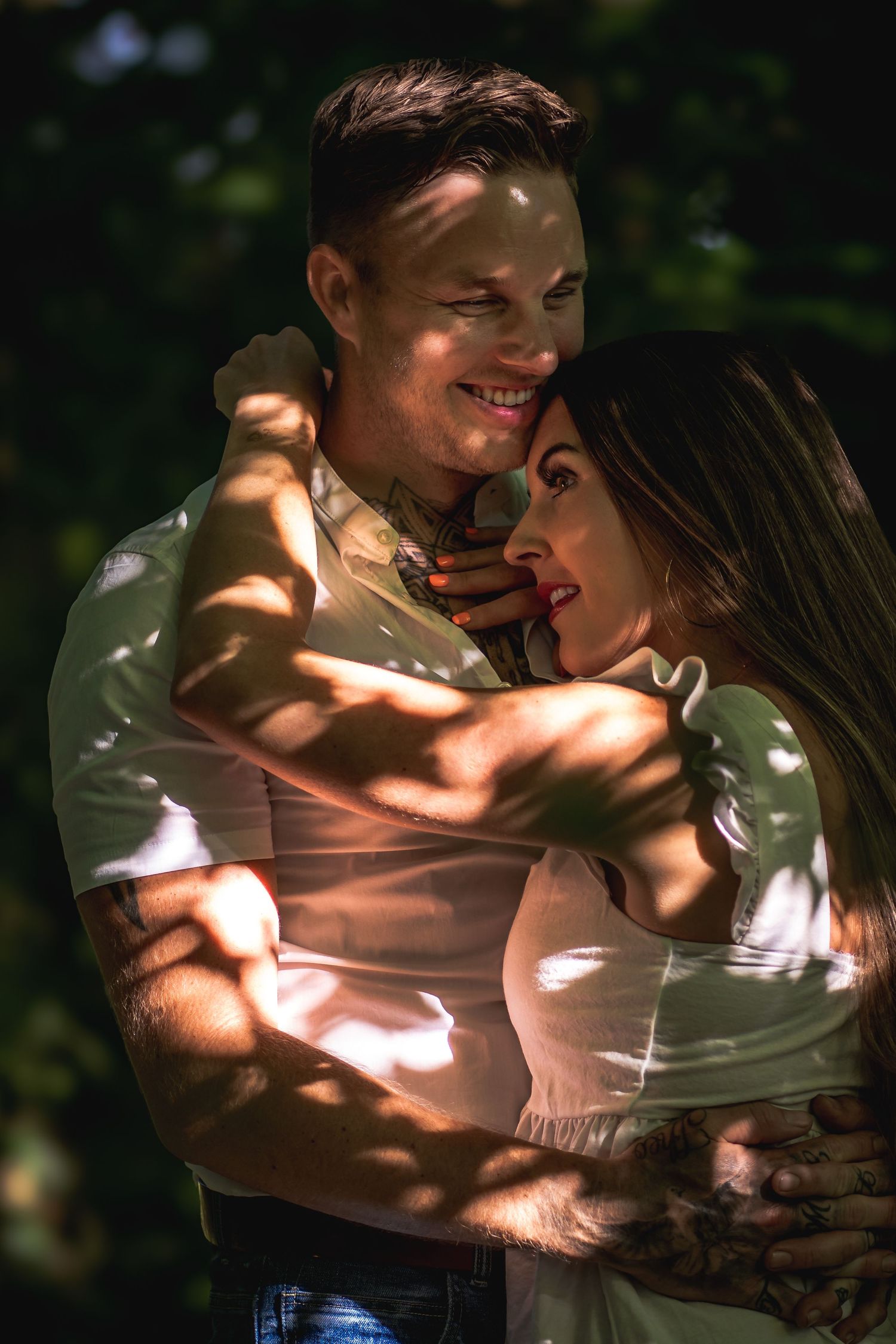 Romantic couple embracing outdoors with dappled sunlight filtering through trees.