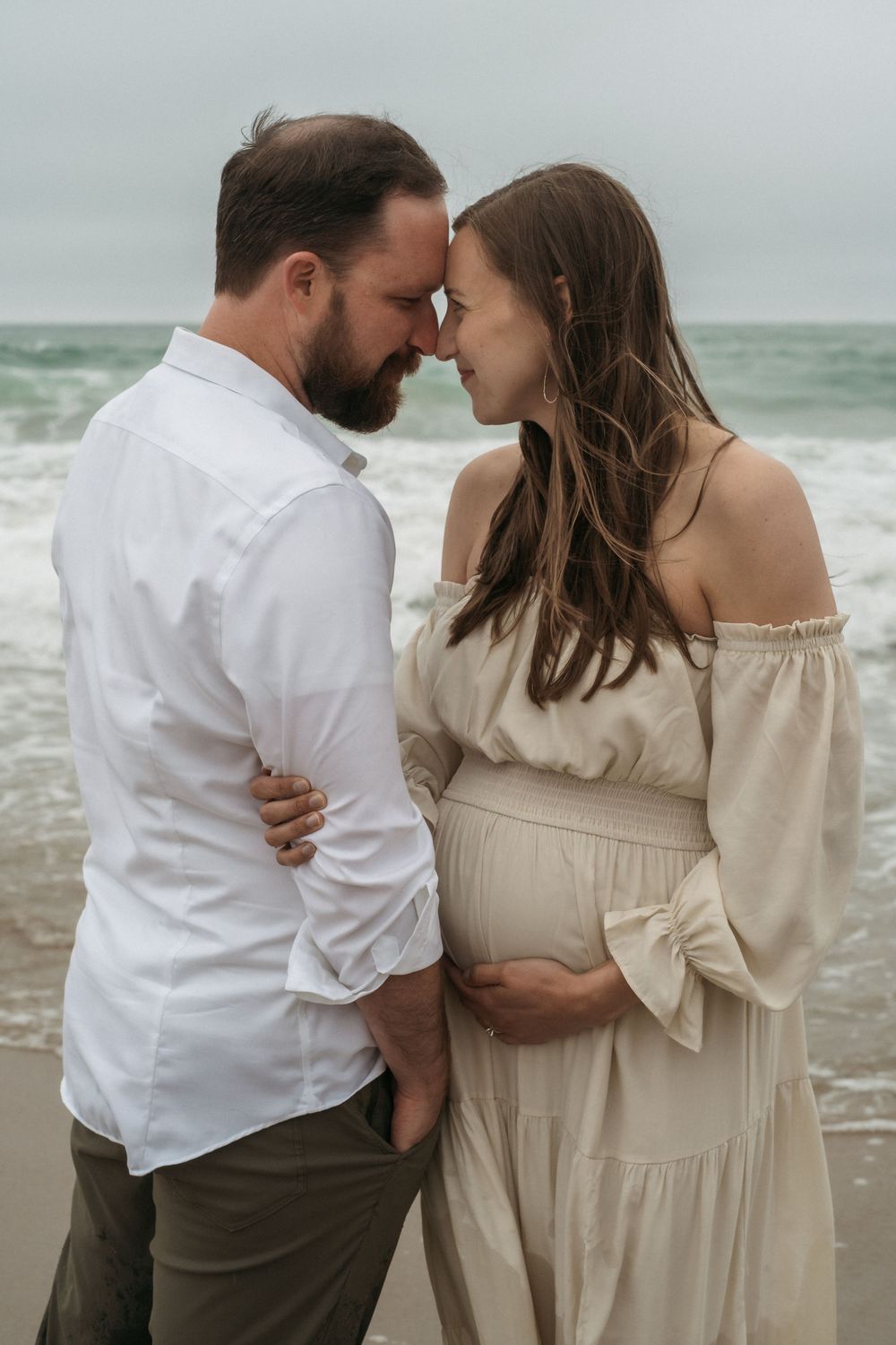 A romantic couple poses tenderly along a misty beach in five connected photos wearing white and beige outfits.