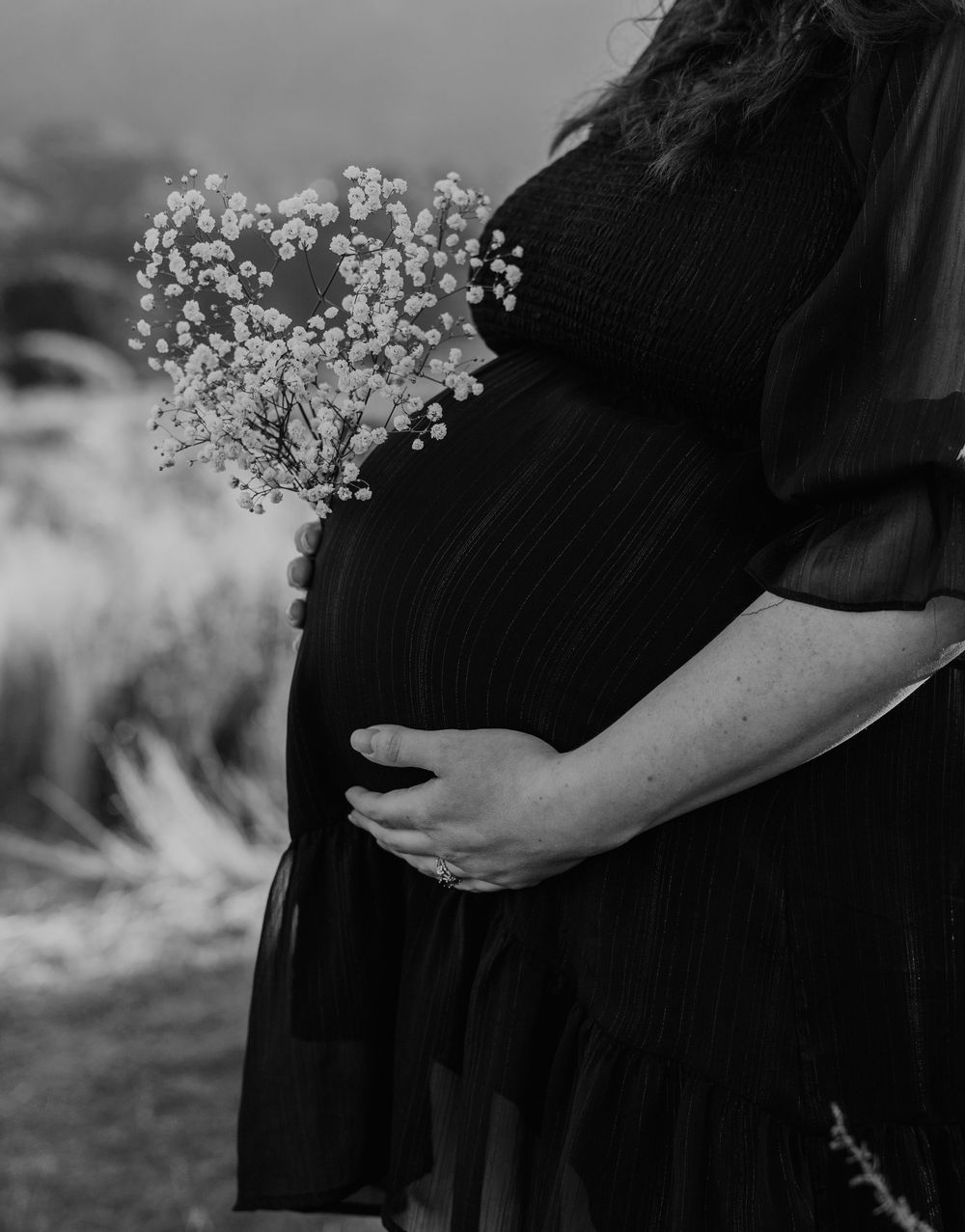 A black and white portrait of an expectant mother holding her baby bump with delicate baby's breath flowers.