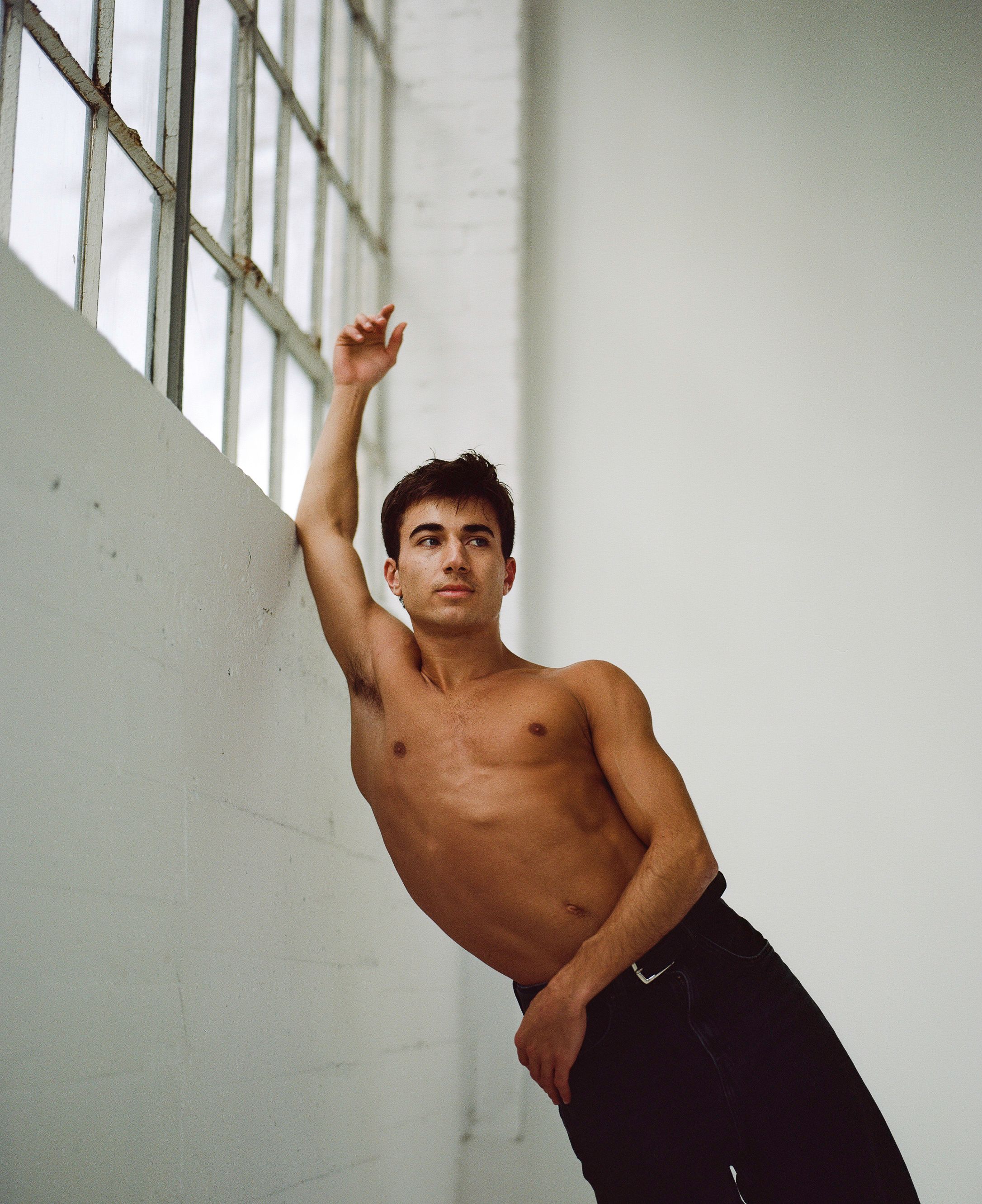 Contemporary dance pose with extended arm against stark white studio wall.