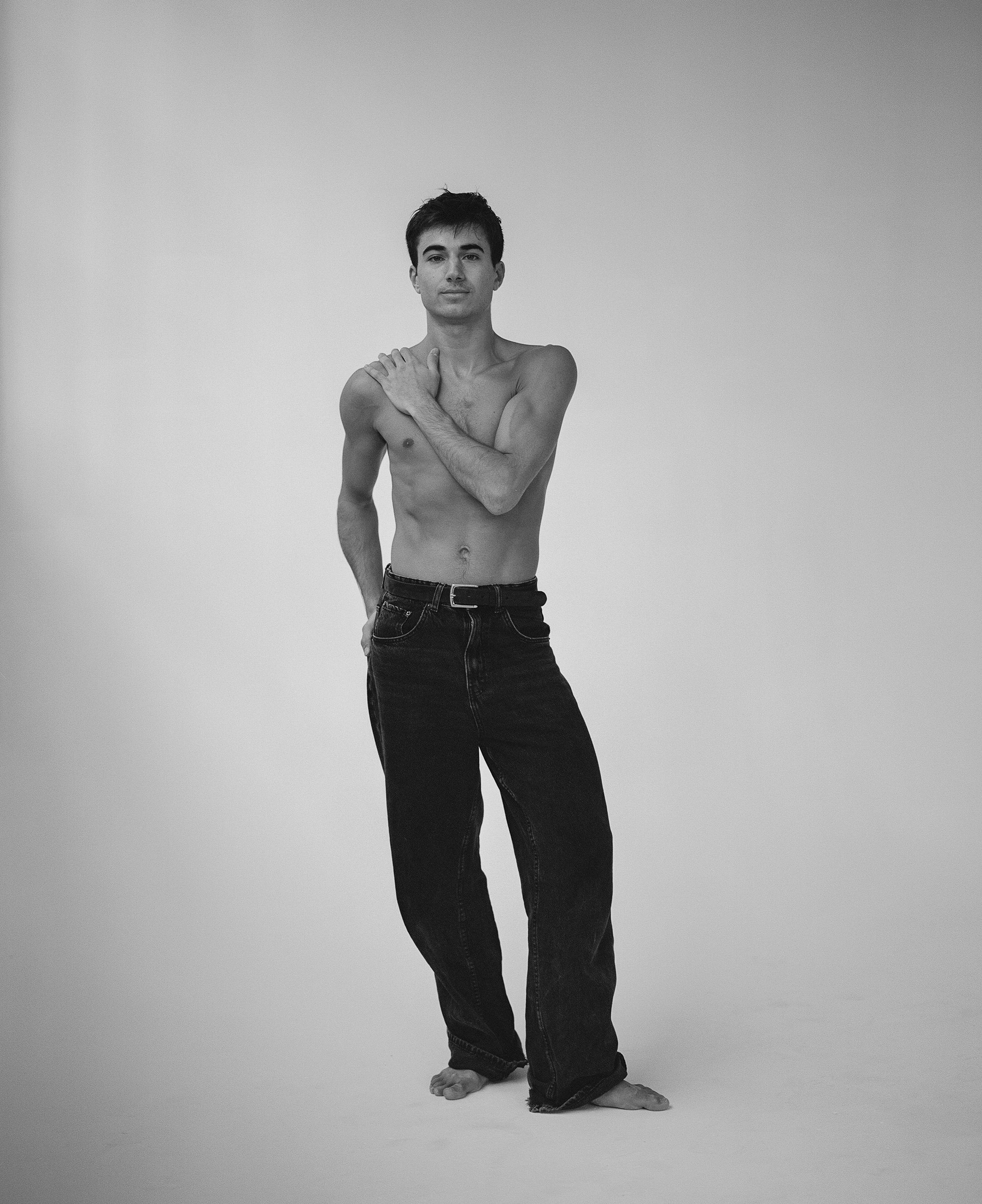 Monochrome studio portrait of dancer in wide-leg jeans against plain background.