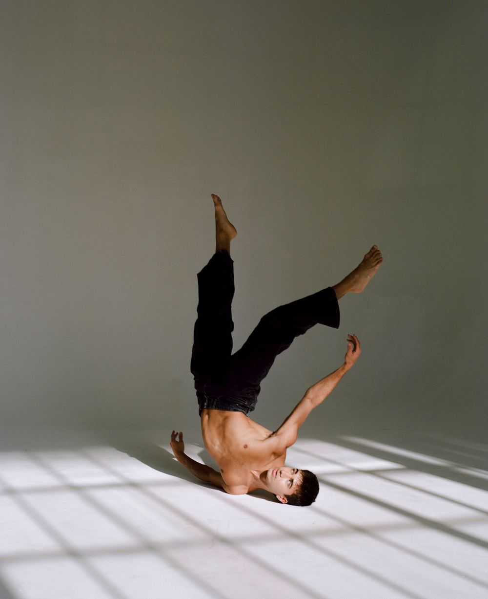 Dynamic headstand dance move performed on light studio floor.