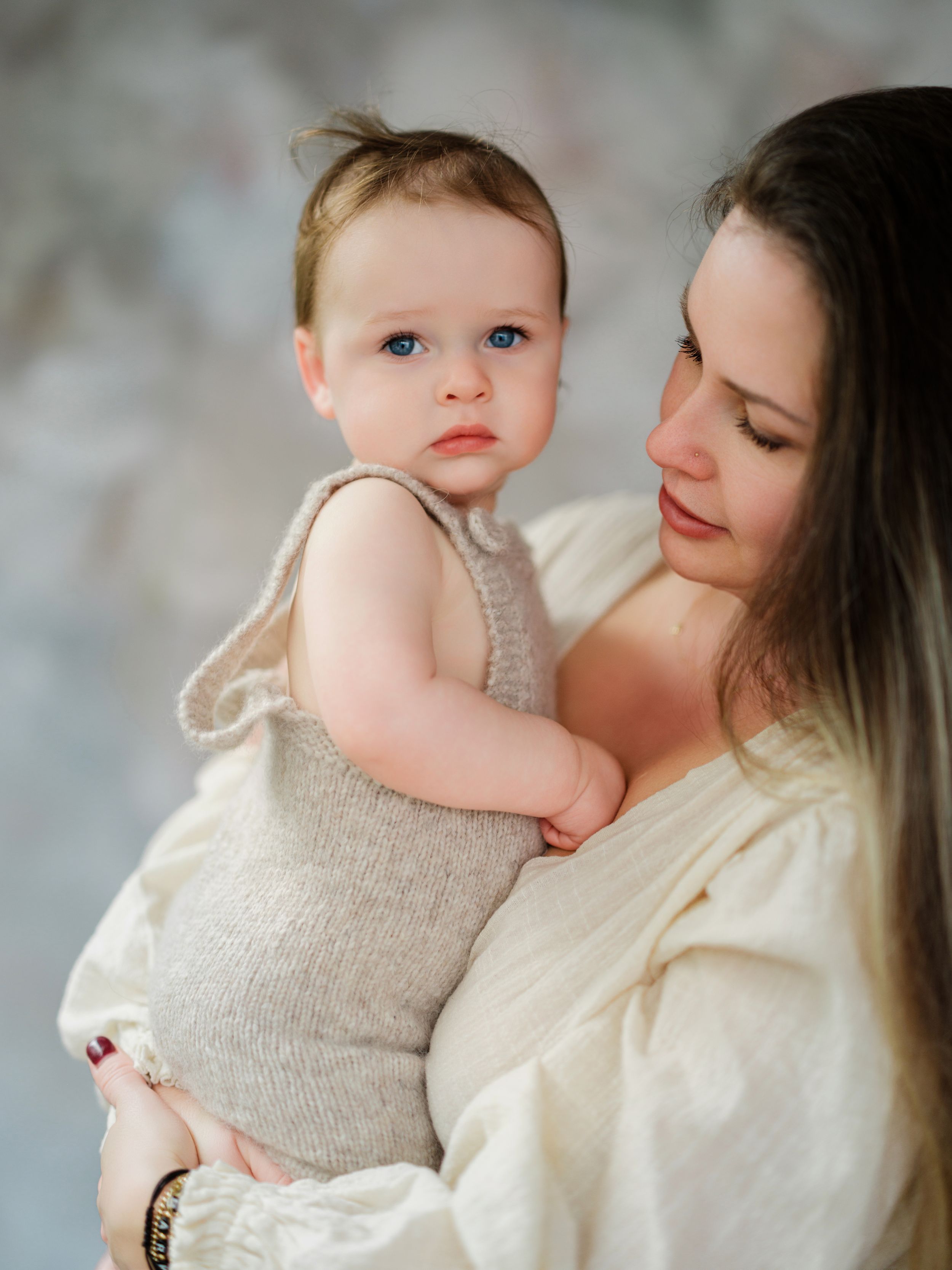 A tender moment between a parent and infant wearing a beige knit outfit against a soft gray backdrop in Bellevue studio.