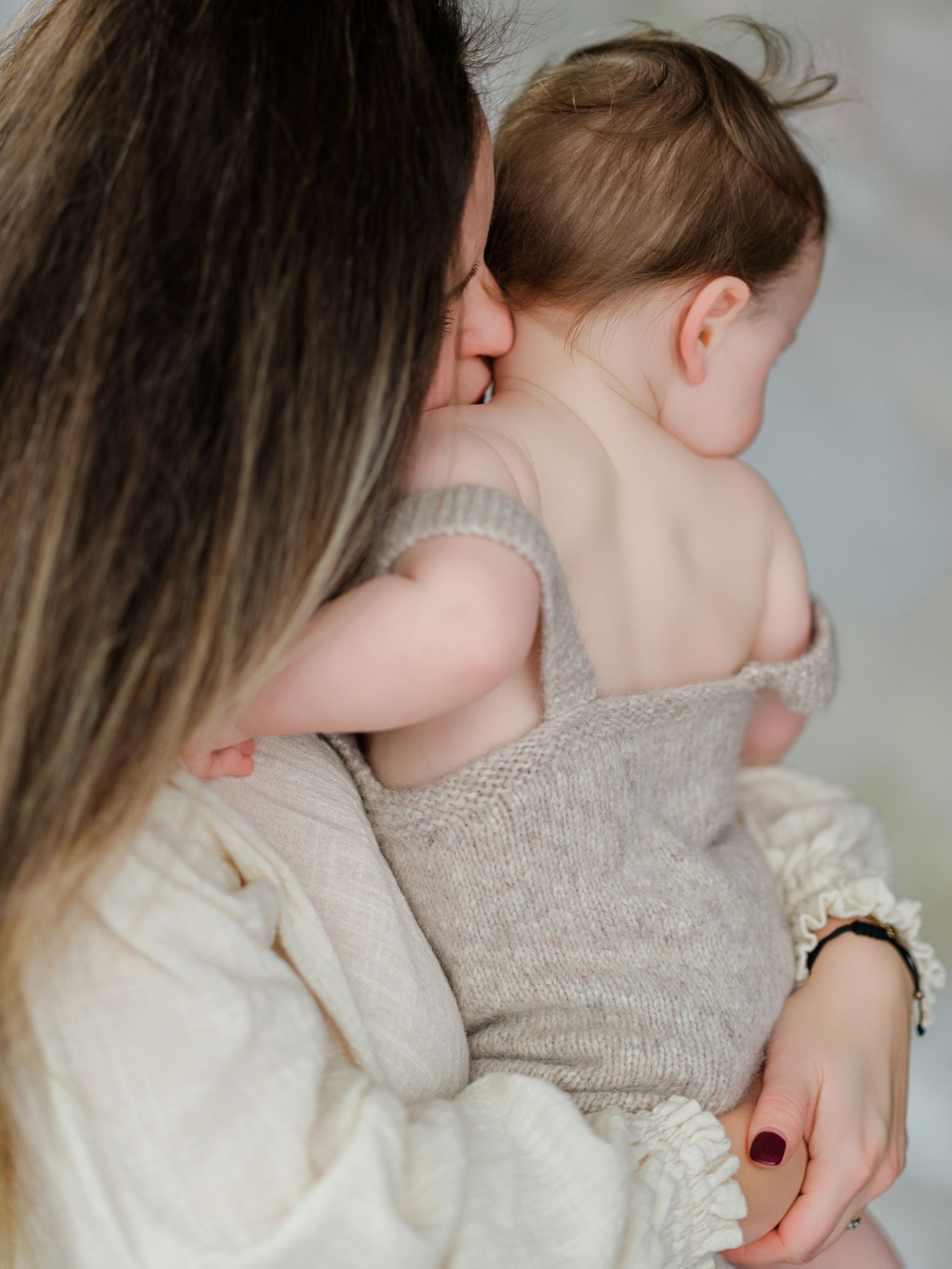 A tender moment between parent and baby wearing gray as they embrace in soft lighting in Bellevue studio.