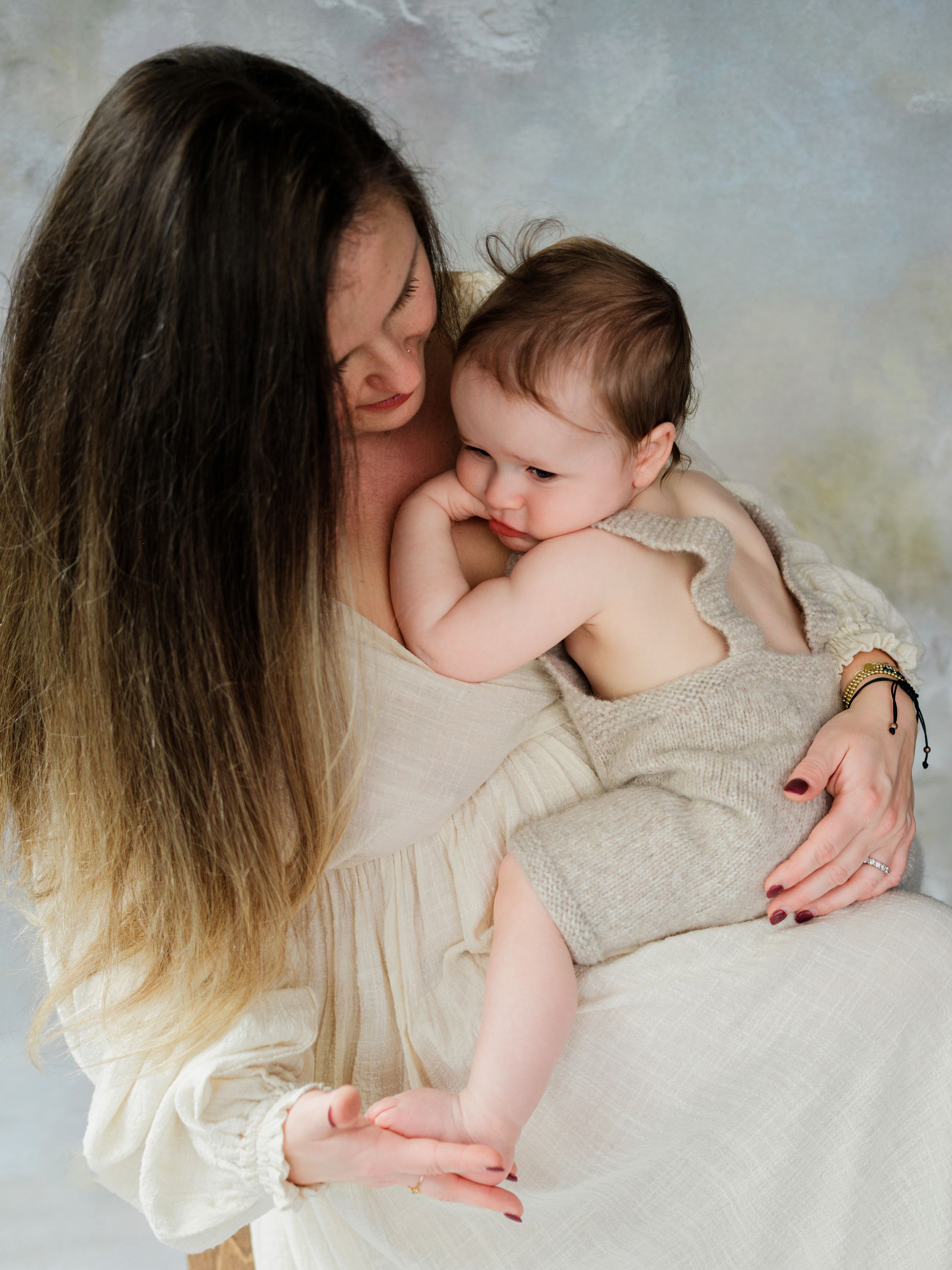 Intimate portrait of parent cradling and kissing a baby dressed in beige against a light background in Bellevue studio.