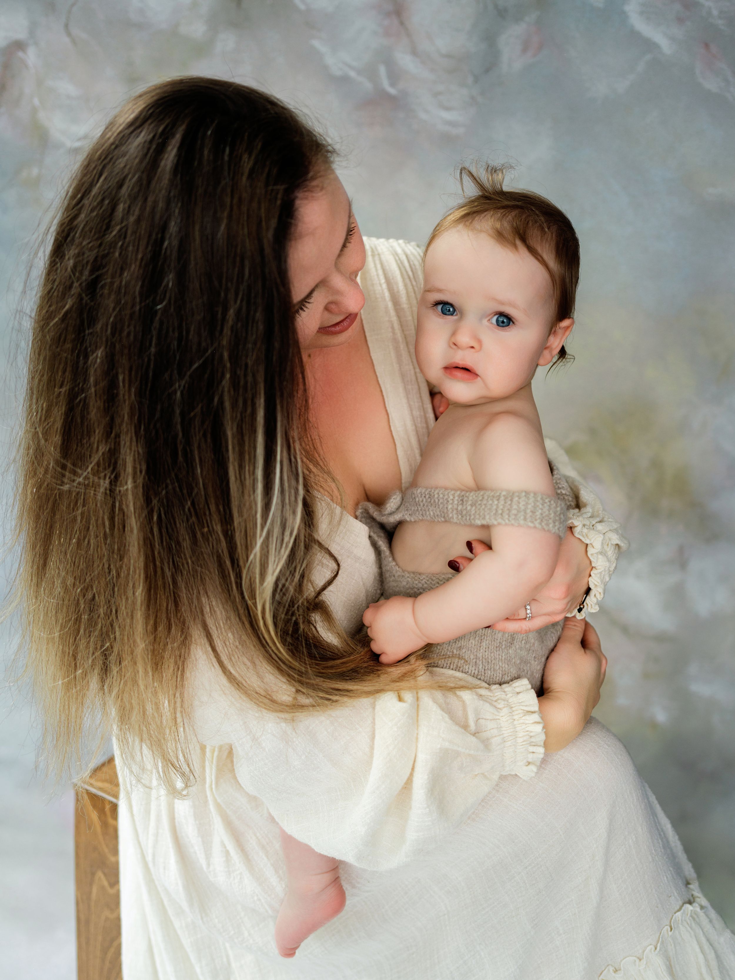 An intimate portrait of parent and baby in soft white clothing against a muted textured background in Bellevue studio.