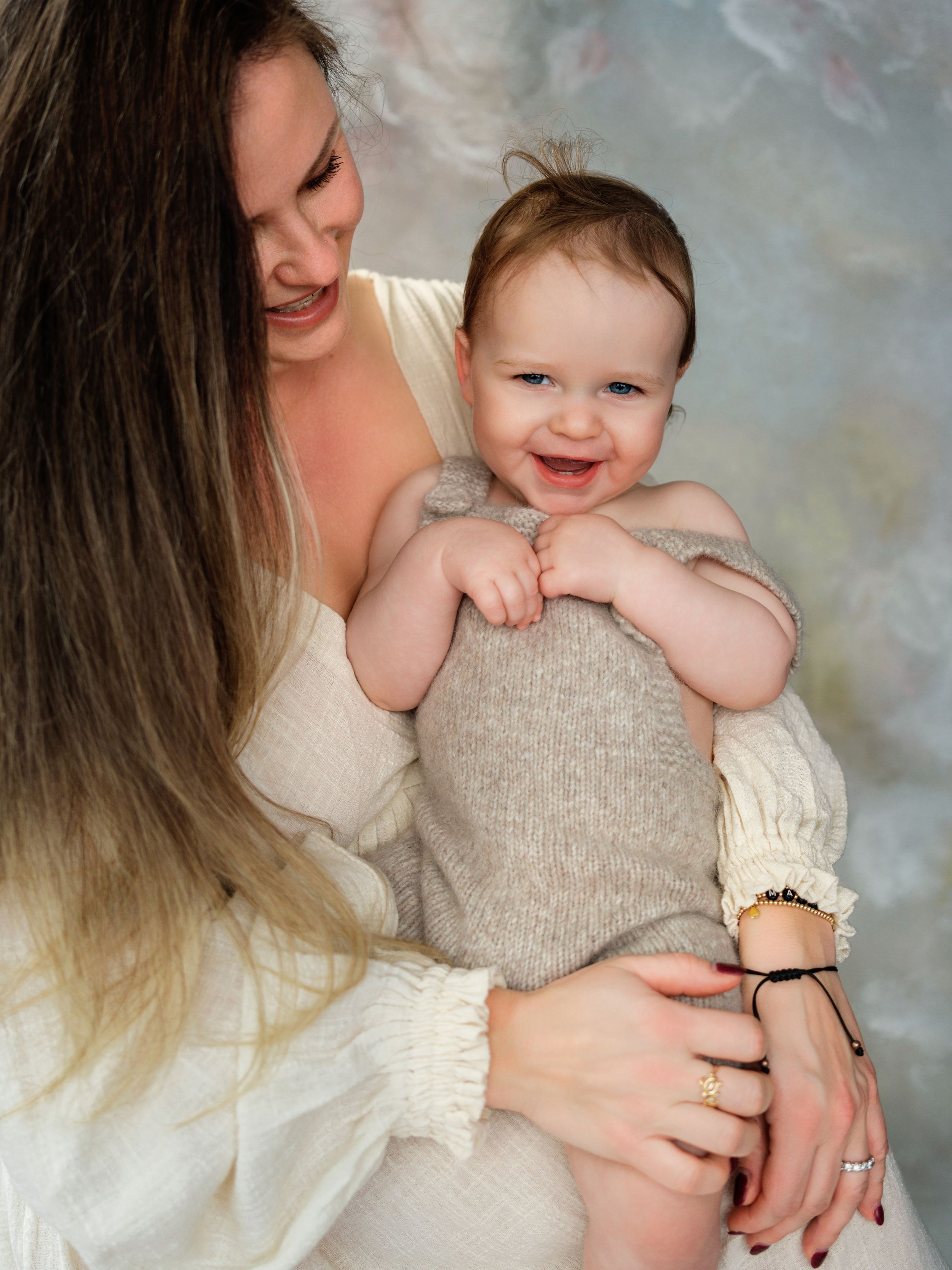 A tender portrait of parent and baby in cream-colored outfits against a soft gray backdrop in Bellevue studio.