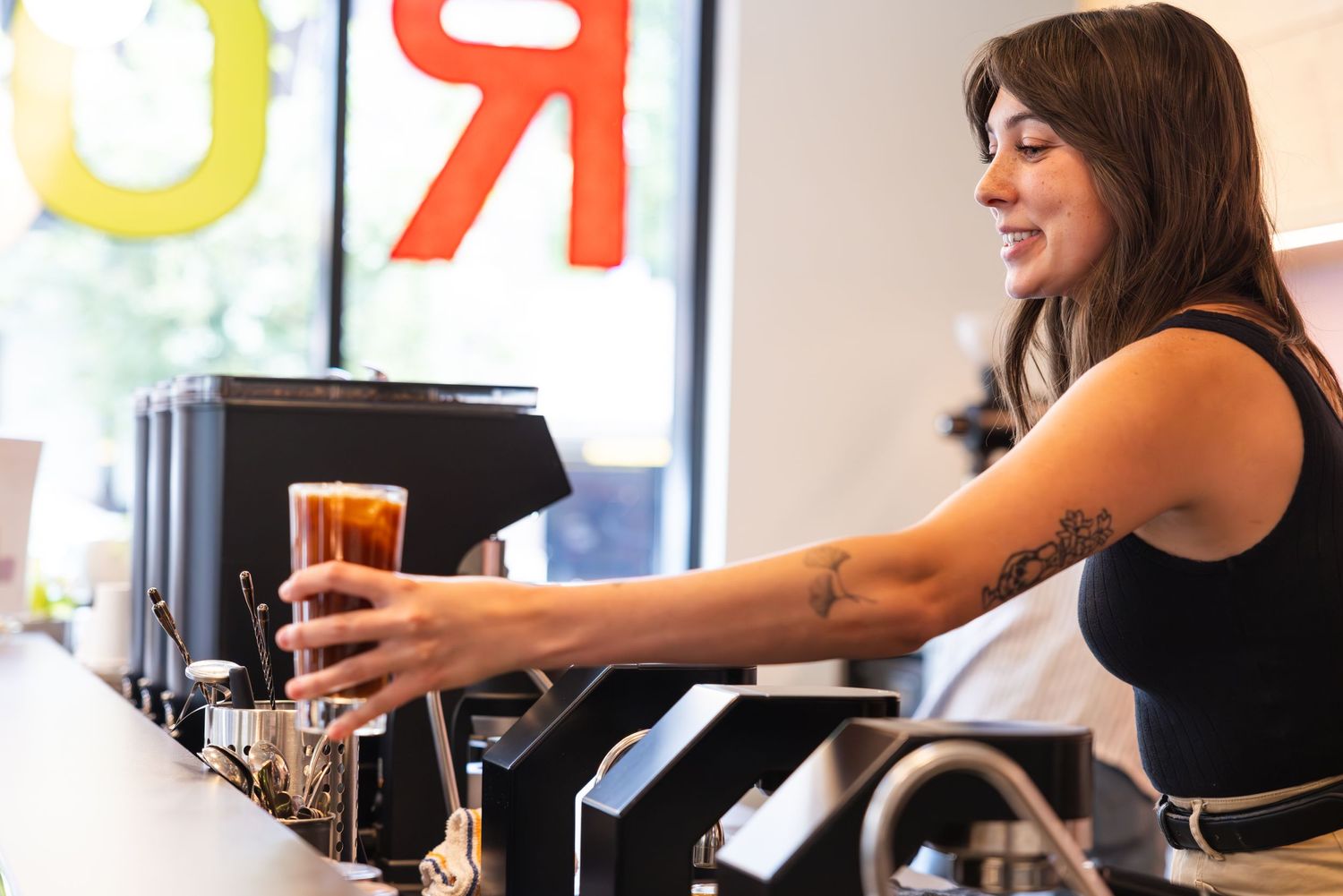A bartender in a black tank top pours a draft beer from the tap at a restaurant bar counter.
