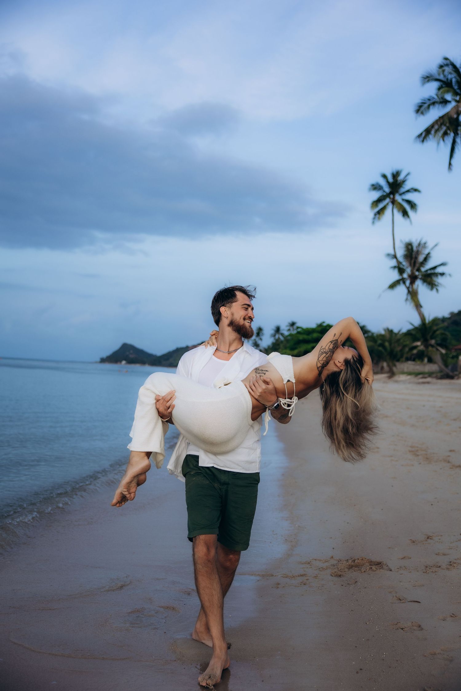 A romantic moment on a tropical beach with palm trees and ocean views during dusk.