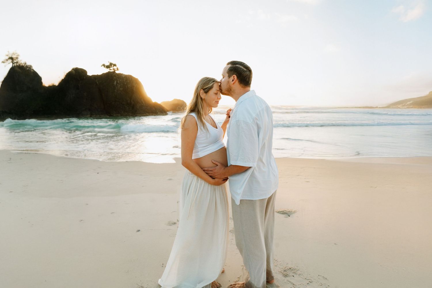 Romantic beach photoshoot at sunset with waves crashing against rocky shore.