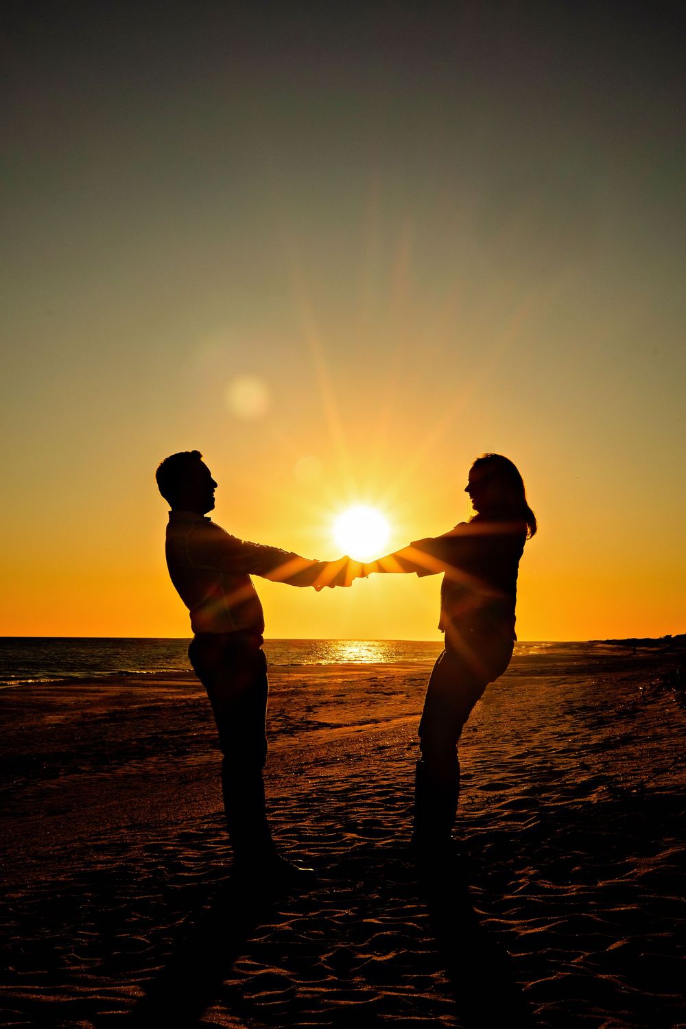 Two silhouetted figures stand against a dramatic orange sunset on a beach, creating a playful sequence of poses.