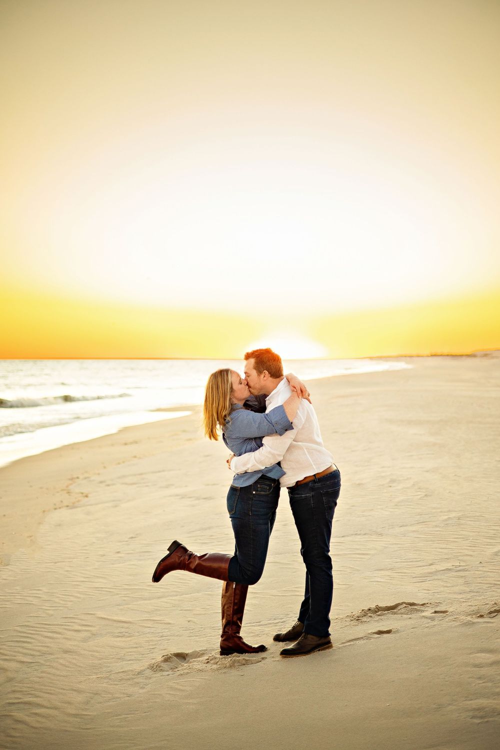 A romantic couple embraces on a sandy beach during golden sunset hour.