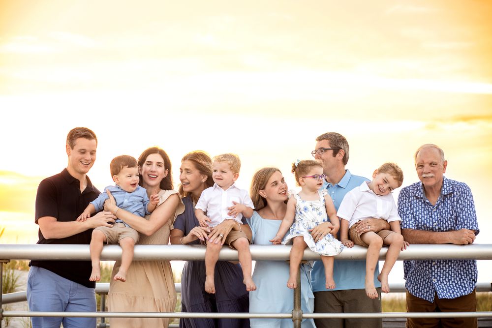A group of people stand together along a railing at sunset, sharing joyful moments in warm golden light.
