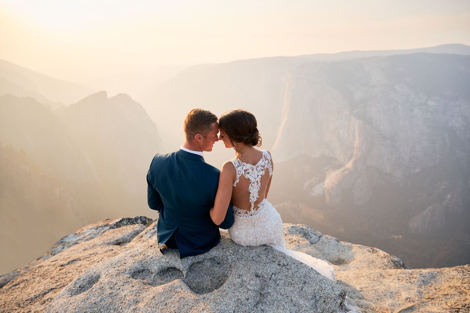 Couple sitting on cliff edge overlooking dramatic mountain vista at sunset. Taft Point, Yosemite National Park