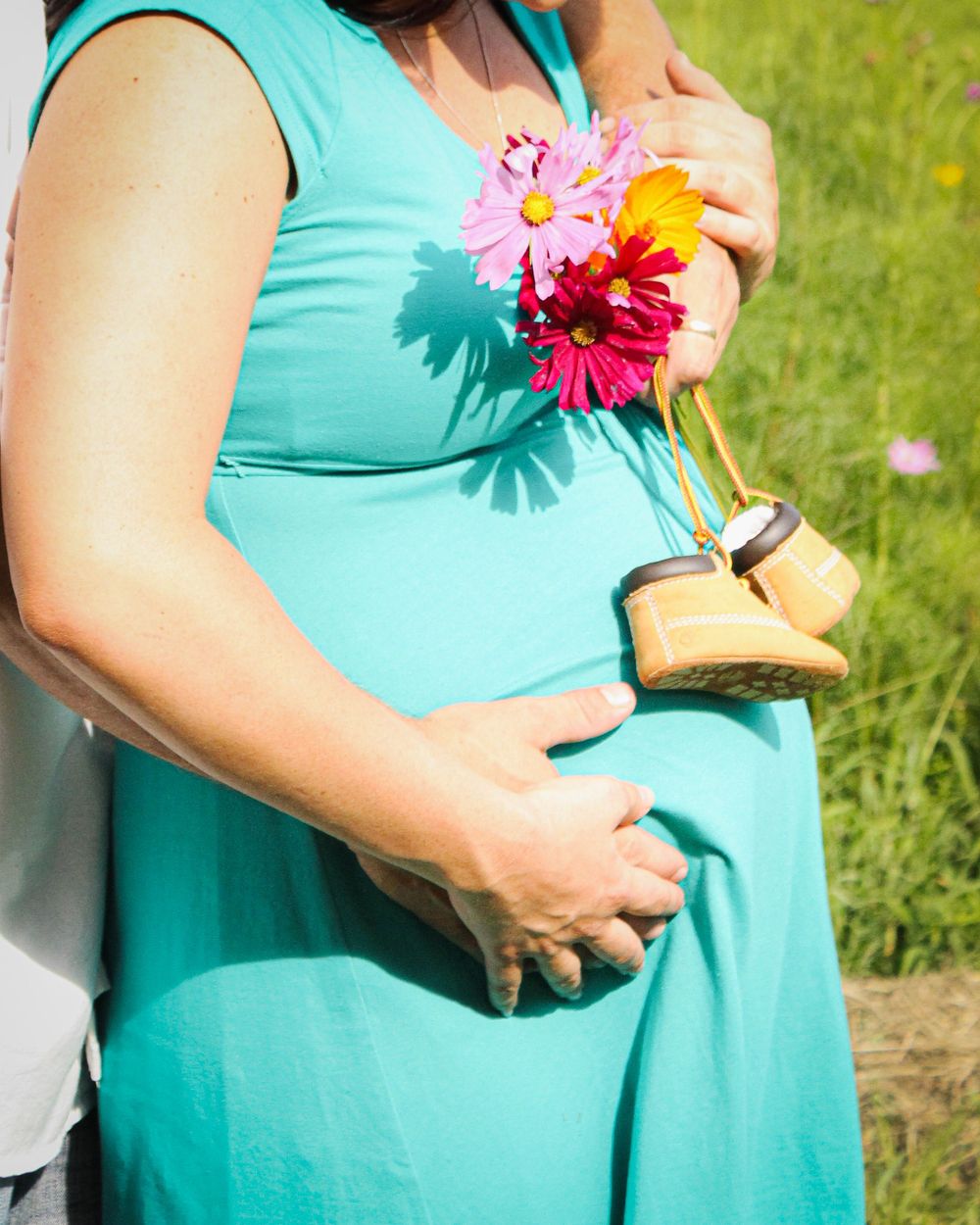 A person wearing a turquoise dress holds a colorful bouquet of flowers while standing in a grassy outdoor setting.