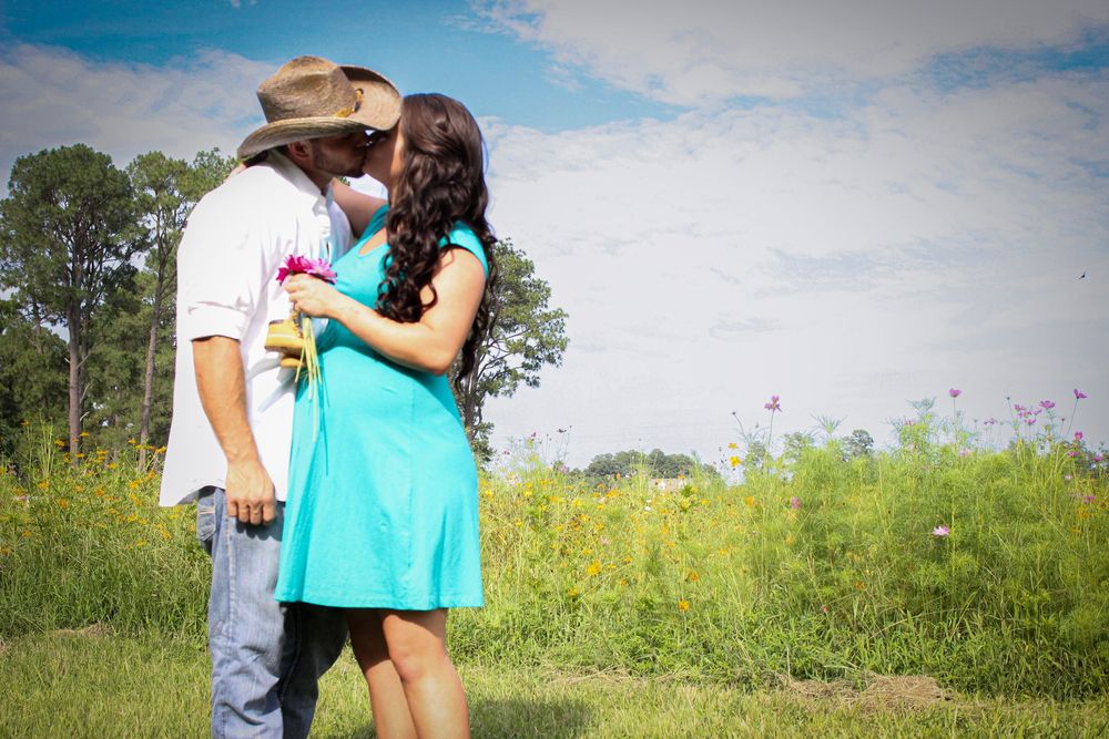 Couple embraces in a field of tall grass and wildflowers on a sunny summer day with blue skies.