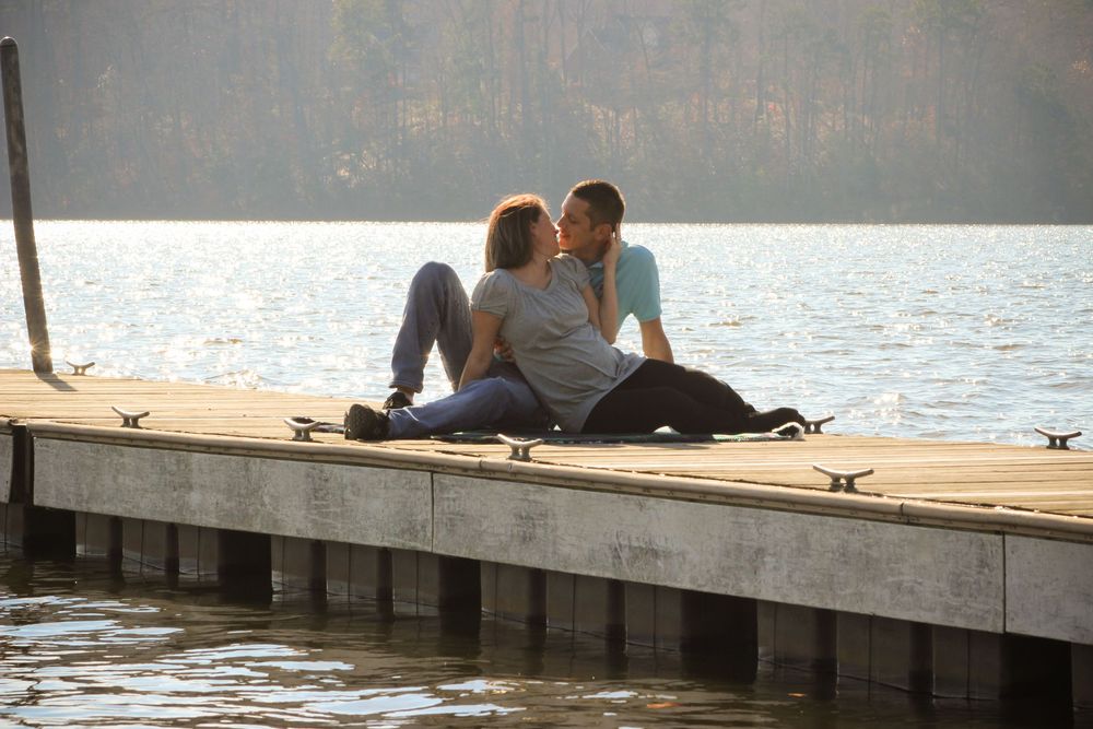 People sit together on a wooden dock overlooking a tranquil lake at sunset.