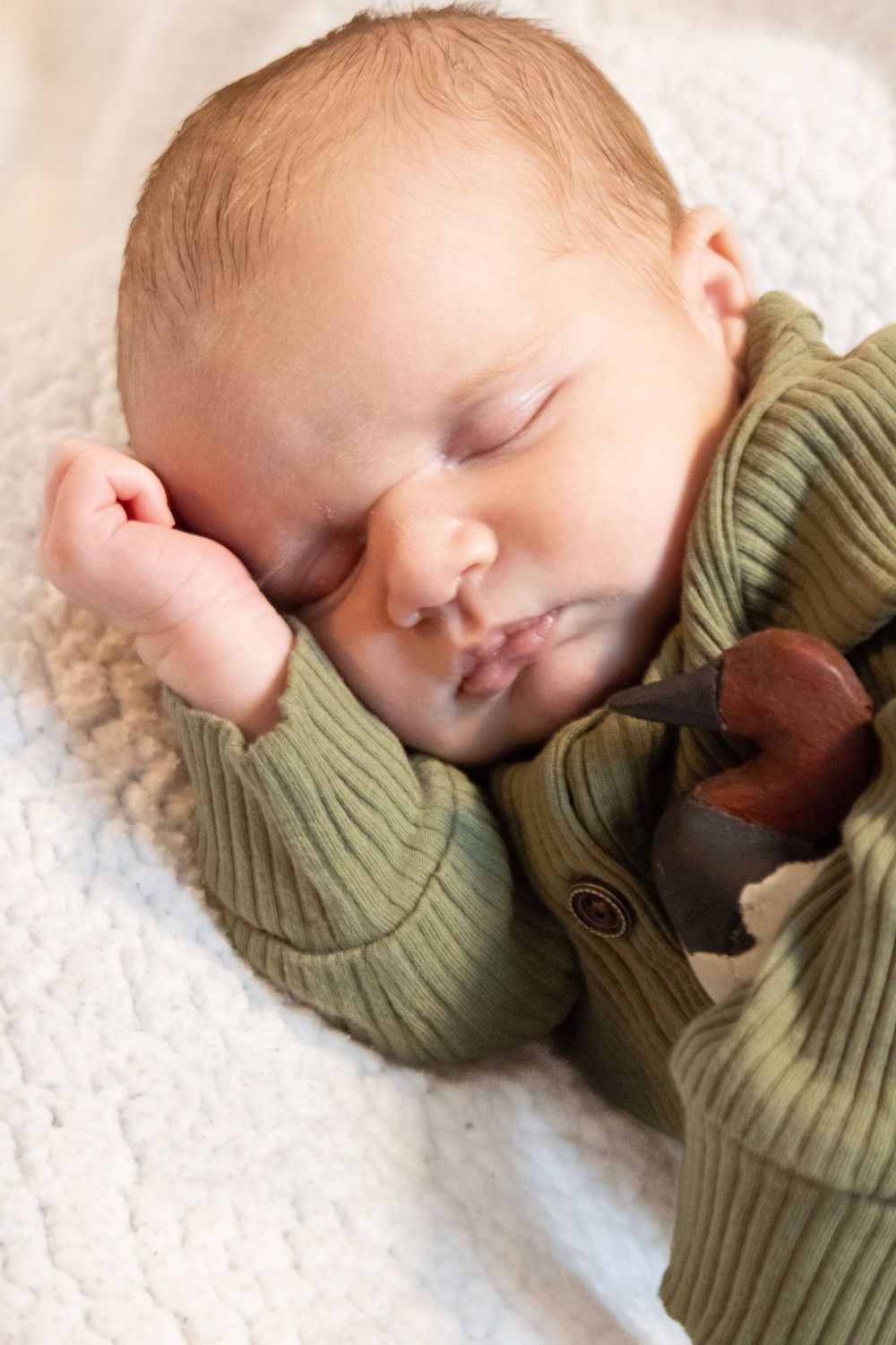 A sleeping baby in a green sweater lies peacefully on white bedding in a series of four similar photos.