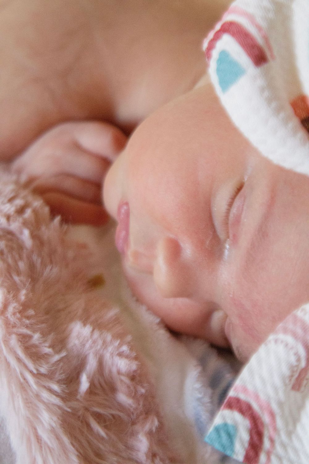 Close-up view of a baby's tiny hand grasping a soft white blanket with delicate details.