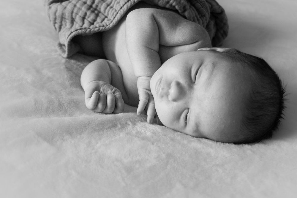 Black and white photo series showing different angles of a sleeping newborn baby in soft natural light.