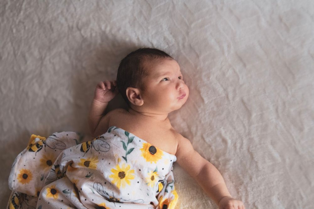 A baby wearing a floral dress lies on a white blanket while looking upward in a series of similar poses.