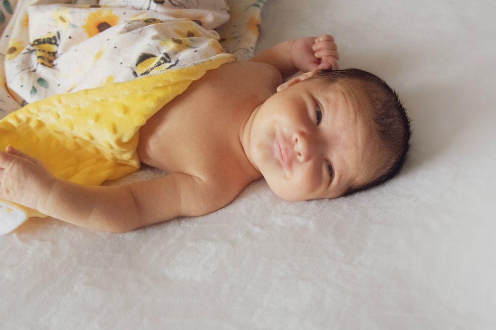 A sleeping baby wearing a yellow dress lays peacefully on a white surface in a series of connected photos.