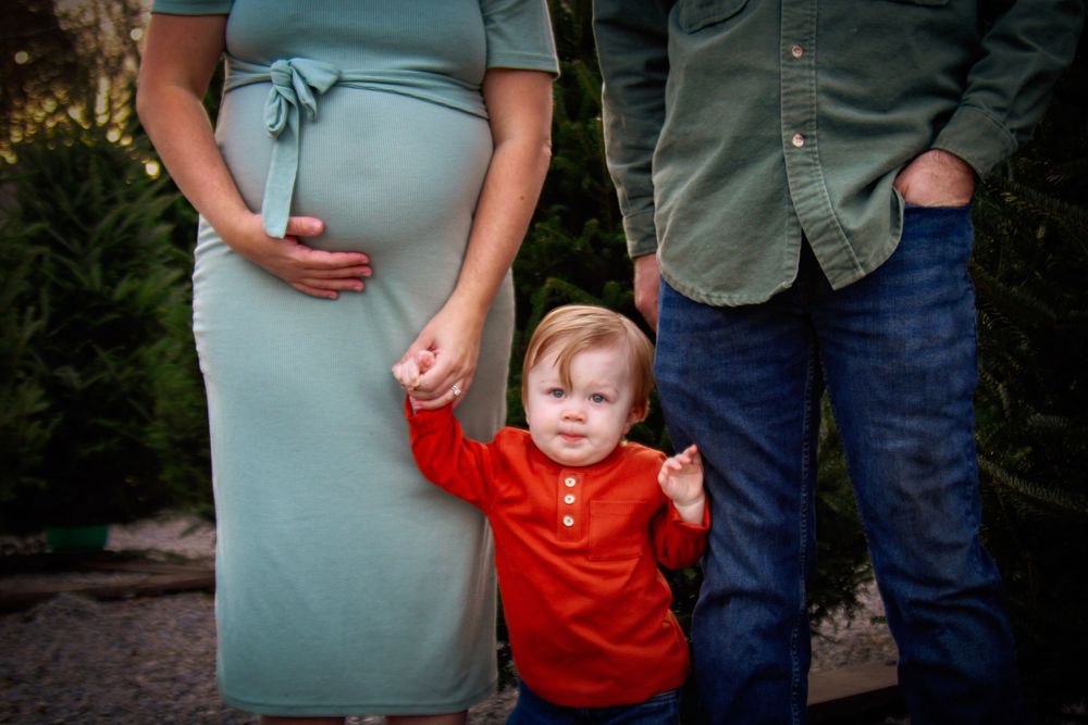 A toddler in red shirt holds hands with parents while standing outdoors.