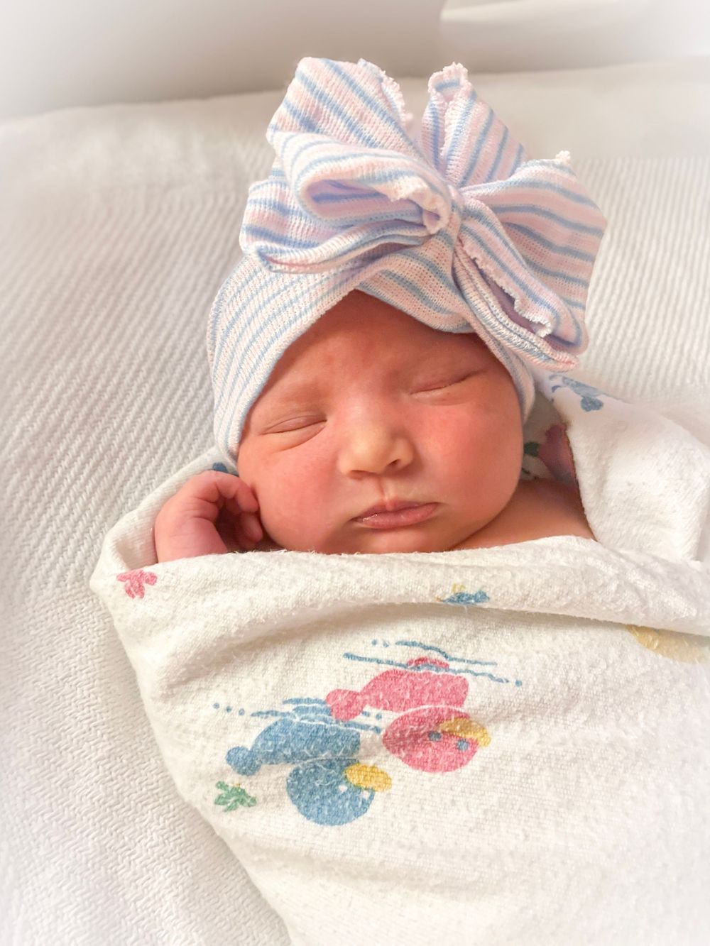Newborn baby sleeping peacefully in white blanket with blue and pink striped bow headband and elephant embroidery.