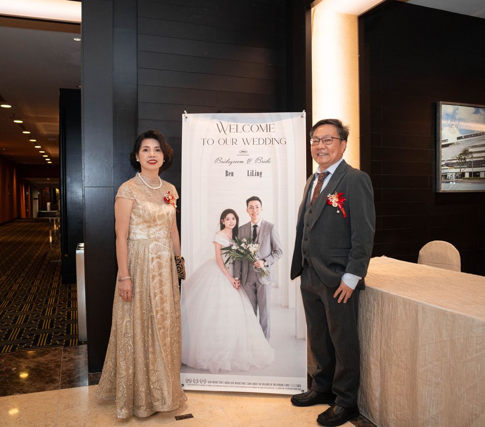 Two people stand beside a wedding banner in an elegant hotel hallway with gold and dark decor.