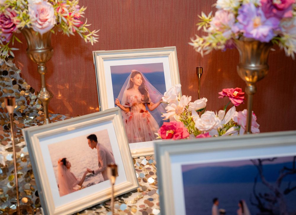 Framed wedding photographs displayed with pink roses and floral arrangements on a wooden table.