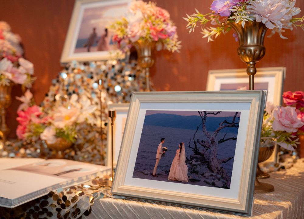 Wedding decor display with framed sunset photo surrounded by floral arrangements and candles on white tablecloth.