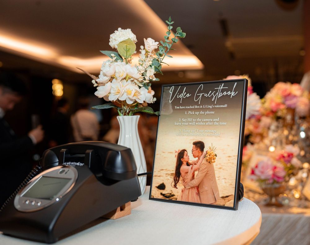 A vintage black telephone sits beside a framed photo display and white floral centerpiece on a reception table.