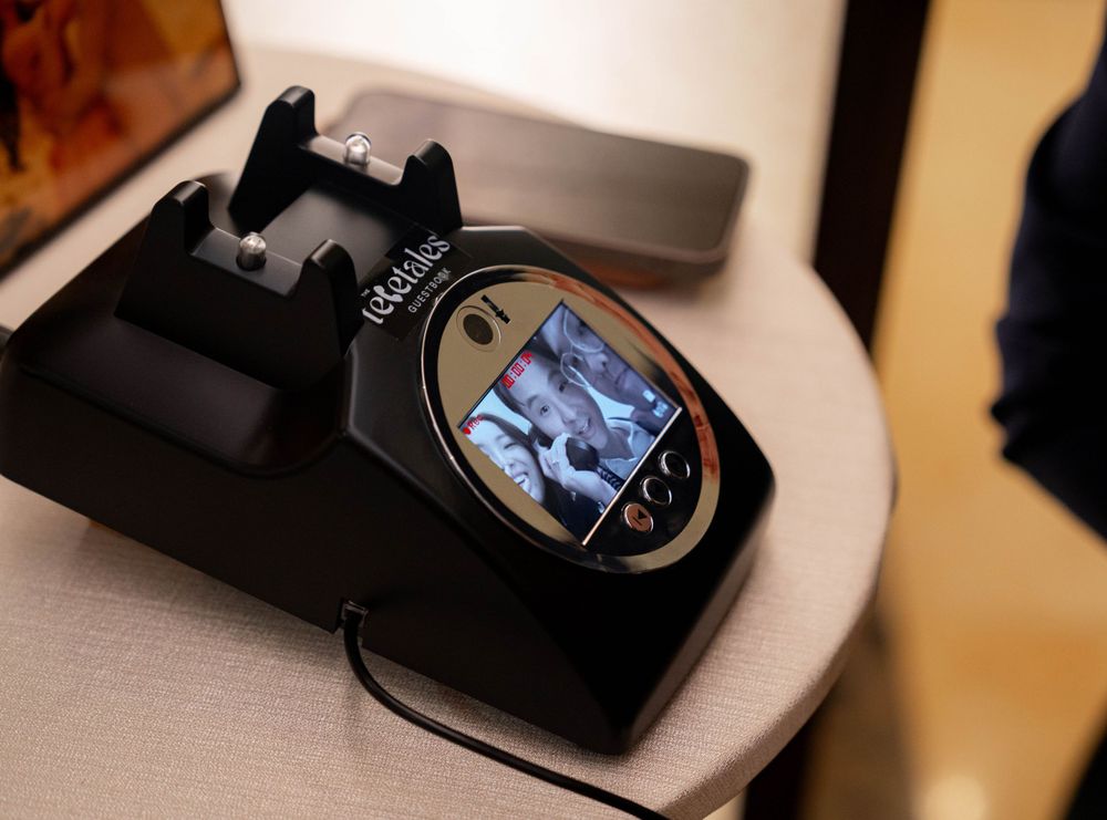 A black digital photo viewer or frame displaying a small blue-tinted image on its LCD screen, sitting on charging base.
