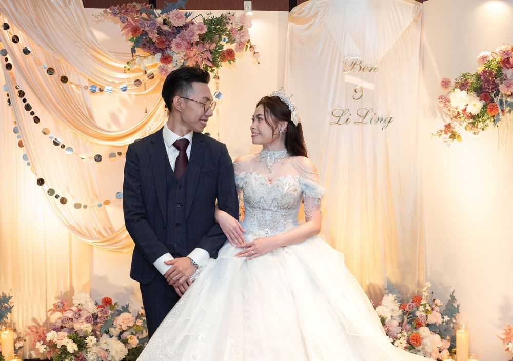 A romantic wedding scene with floral decorations and white drapery features a couple on stage.