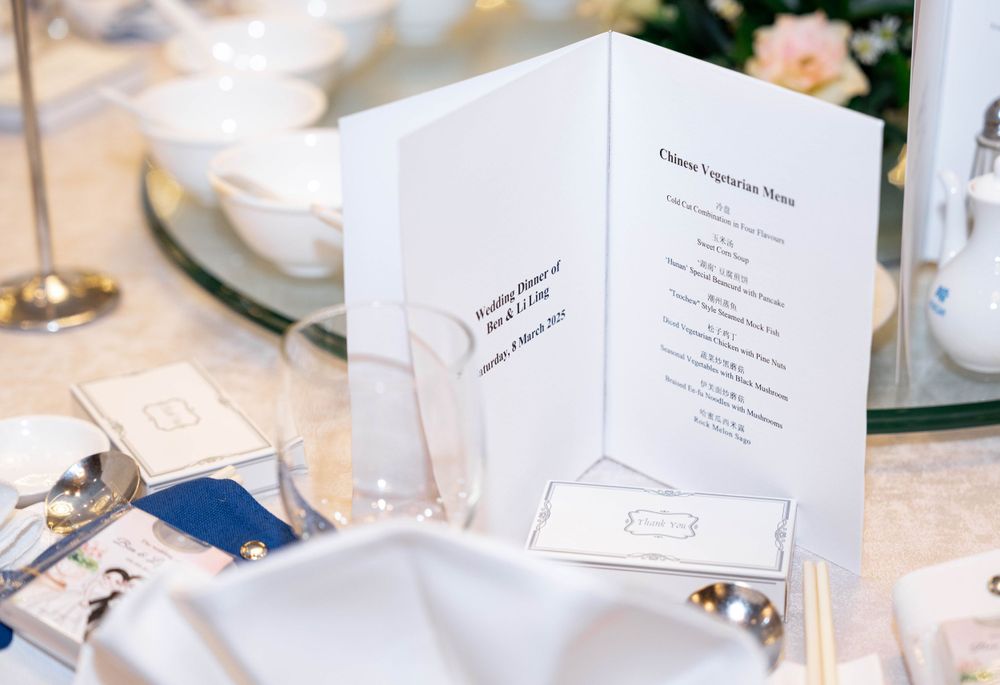 White wedding menu card displayed on elegant place setting with blue napkin and formal dinnerware.