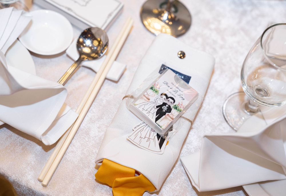 A vintage-style wedding napkin with gold cutlery and glassware on an elegant white table setting.