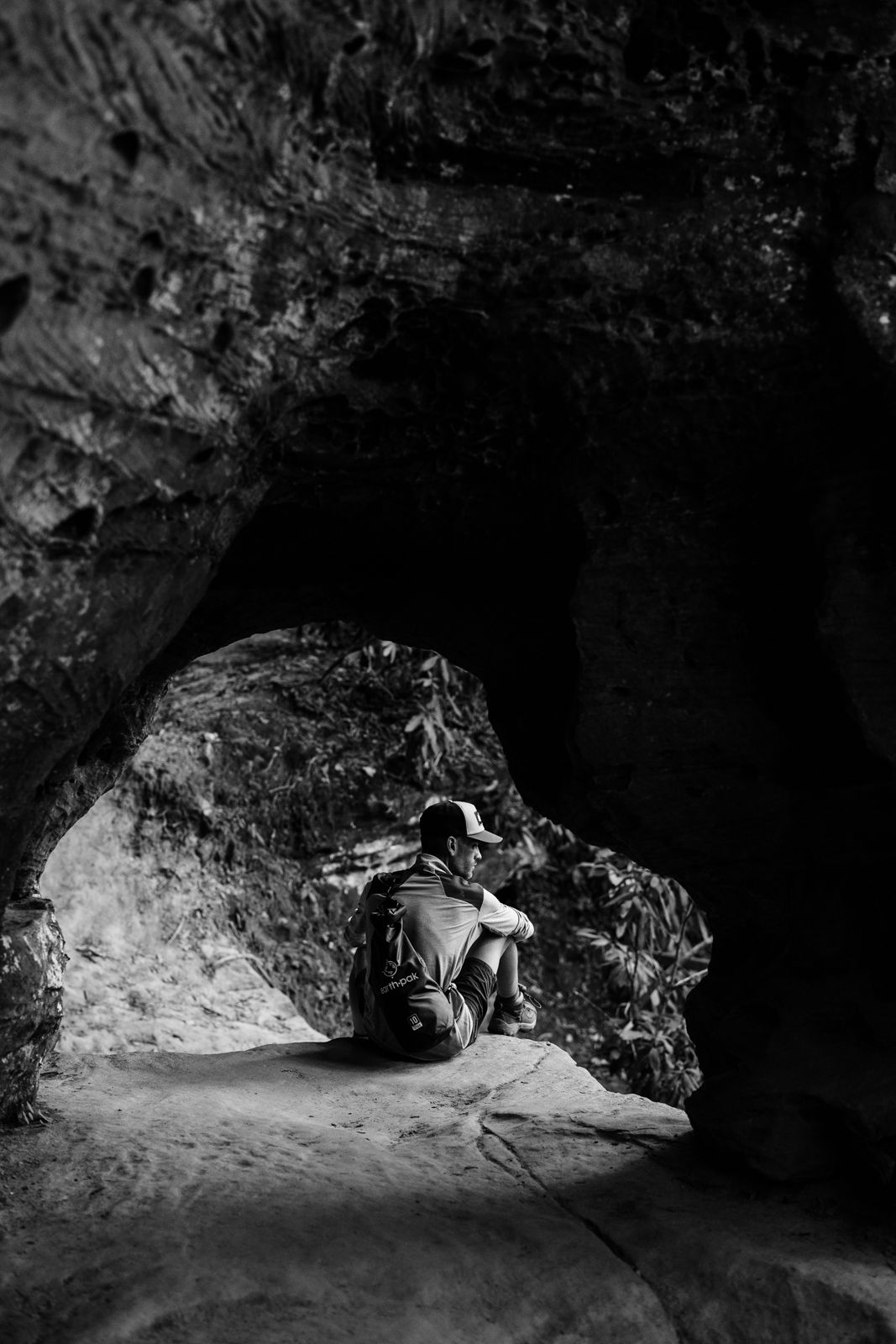 Red River Gorge Hiking | A lone explorer sits in a dark cave opening illuminated by natural light.